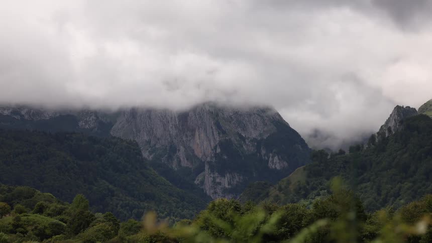 A timelapse captures fastmoving clouds and fog swirling over a majestic forestcovered mountain peak on an overcast day