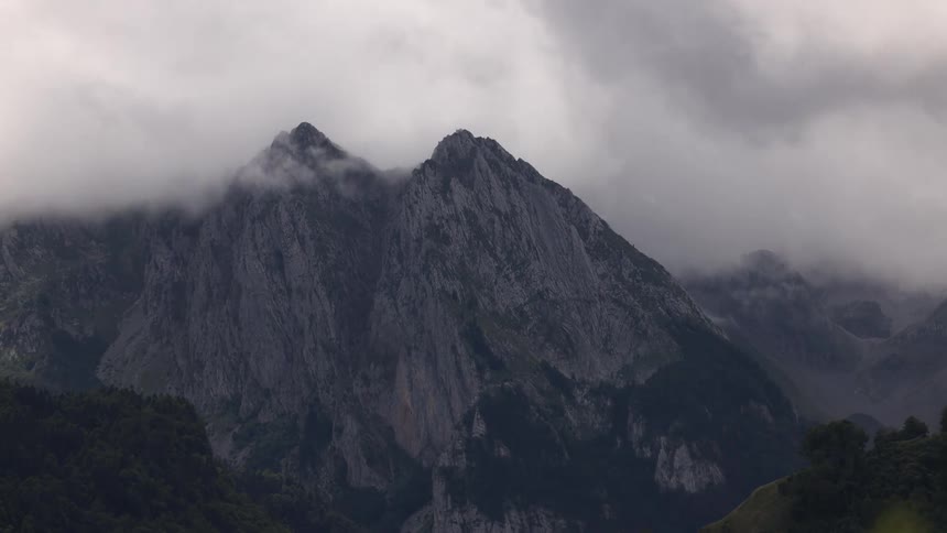 Rocky mountain covered with vegetation and partially surrounded by clouds