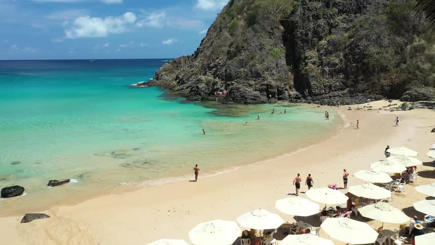 A group of people enjoying themselves on the beach at midday laughing and playing under the bright sun