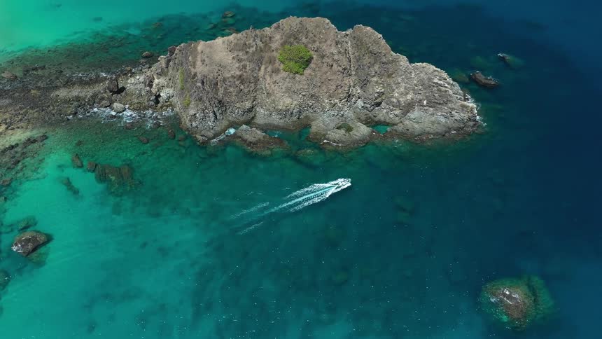A boat sails along a rocky coast at midday