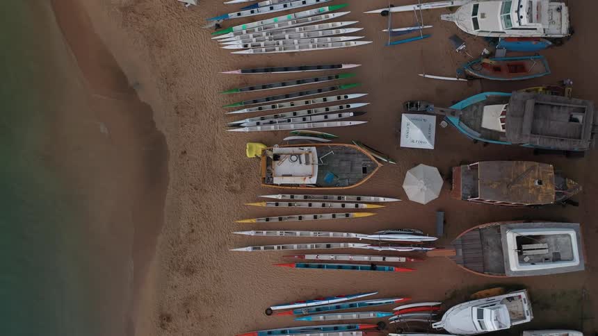 A drone shot from high above shows a sandy beach littered with a wide variety of boats including small canoes and kayaks an old derelict wooden boat and several white yachts