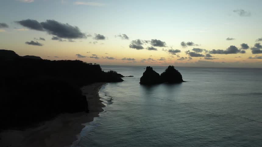 A rocky coast at sundown with waves creating a ripple effect on the water