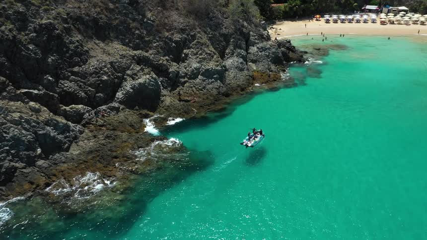 Boat sailing near a rocky shore with a light sandy beach in the background