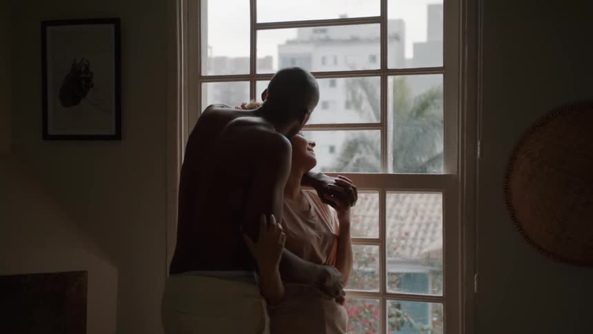 A couple stands by the window hugging each other in the living room at midday