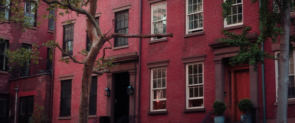 Trees line the street in front of red brick townhouses on a summer day