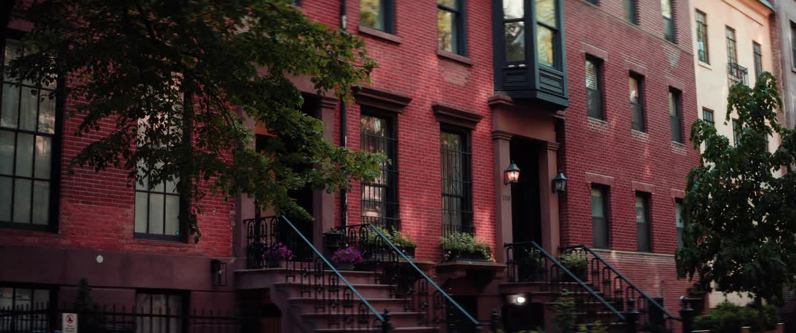 A wide shot of a row of brick townhouses is shown with a tree in the foreground the camera pans from left to right showing the details of the buildings