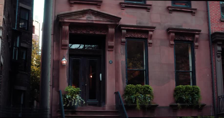 The facade of an ornate brownstone townhouse features a recessed front door large windows with decorative trim and lush window boxes