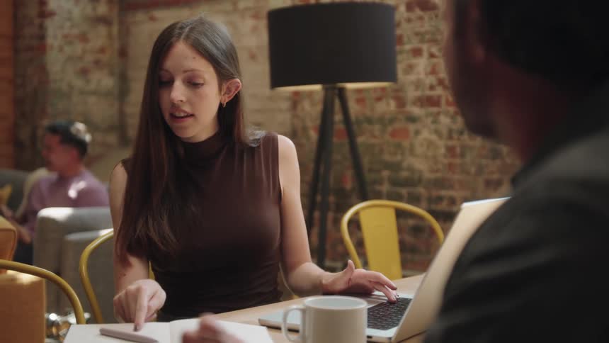 Woman and a man sitting at a table with laptop talking