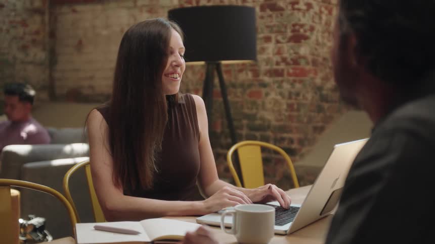 Man sitting at a table talking to a young woman who is typing on a laptop