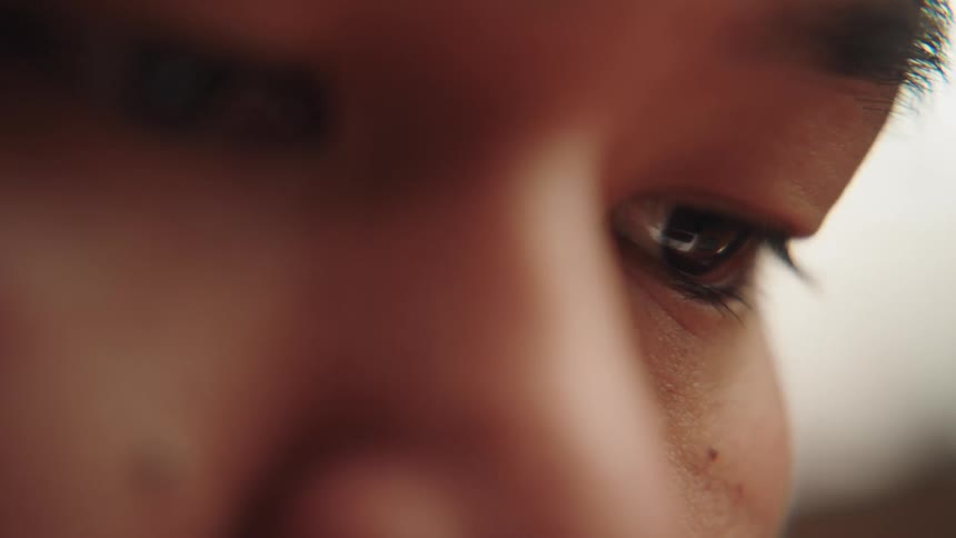 Asian person blinks with their eyes looking slightly down