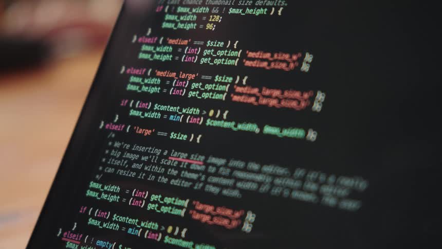 Hand holding a pen pointed at colorful lines of code on a screen
