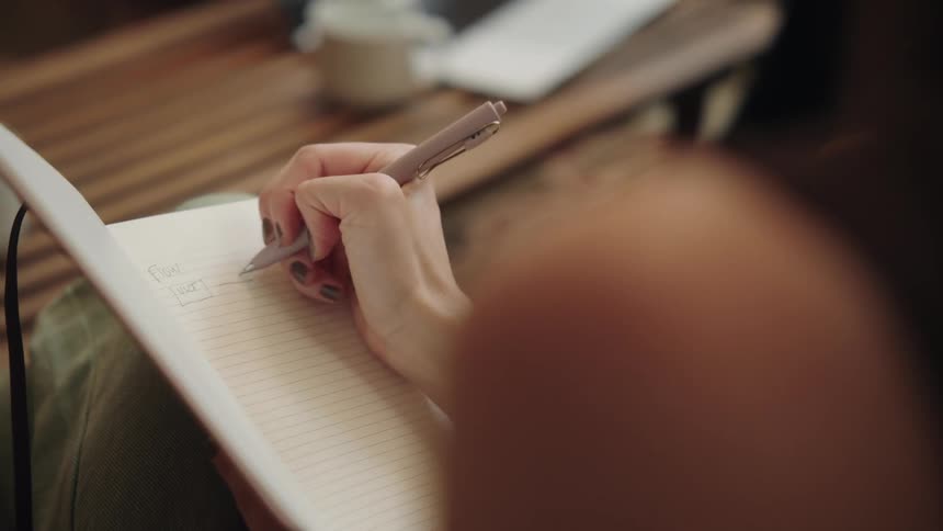 A shot from above shows a person writing in a notebook with a pen their hand moves across the page as they jot down some notes