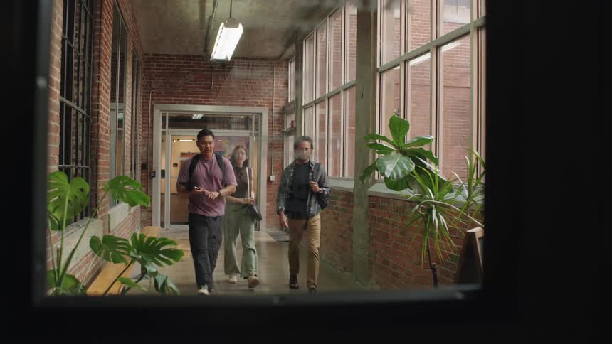 A diverse group of colleagues are seen walking down a brightly lit hallway probably from an university engaging in a conversation