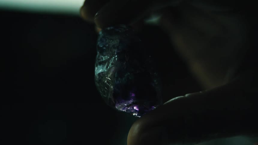Hand holding a translucent purple crystal in a dark environment