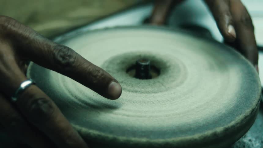 A persons hands are shown turning and polishing a spinning disc with another disc they are wearing a ring on their finger