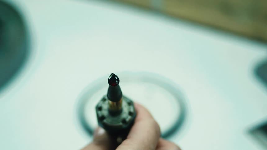 Man performing lapidary work uses a tool to hold a gem while examining it