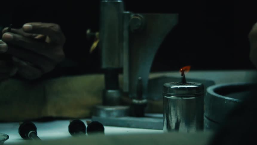 Male hand holding a tool near a lit burner on a workbench