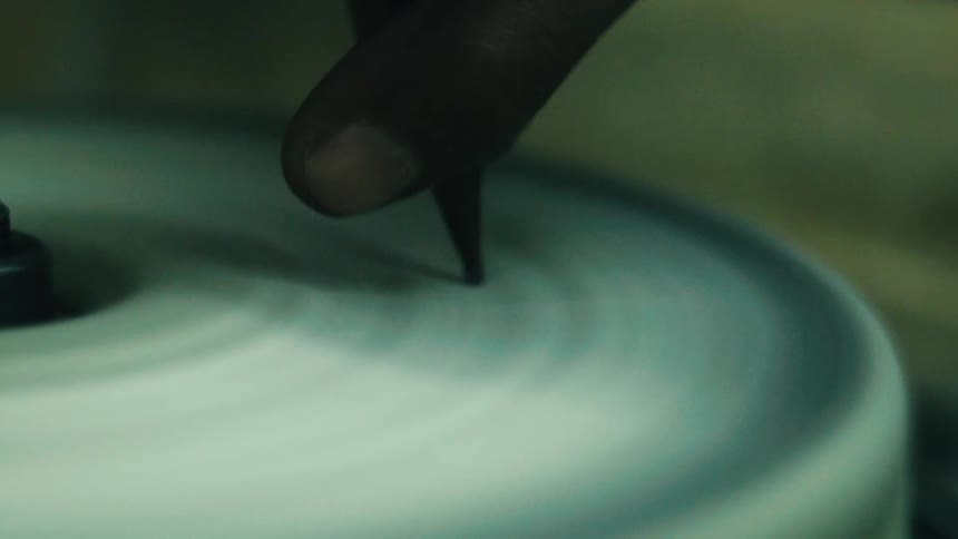 A man is using a polishing wheel to polish a small stone or a gemstone he holds the stone with a tool and presses it against the spinning wheel to grind and polish it the work is done on a table with a spinning disc in the middle