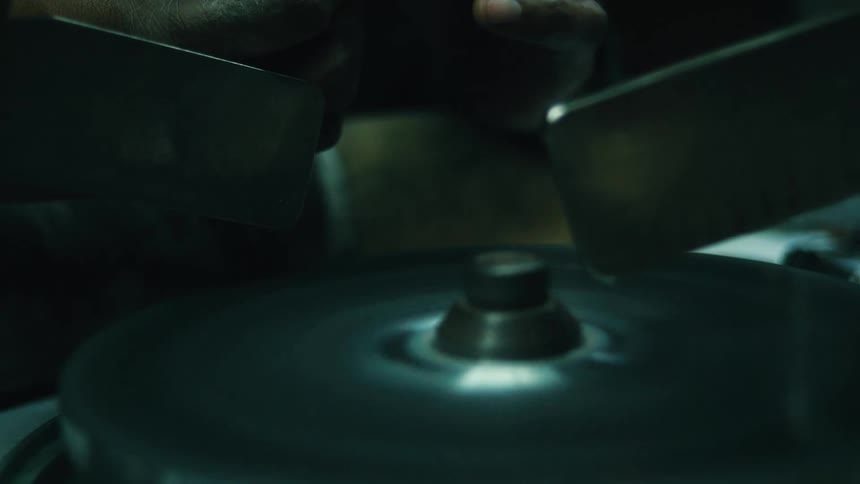 A man is using a polishing wheel to polish a small stone or a gemstone he holds the stone with a tool and presses it against the spinning wheel to grind and polish it the work is done on a table with a spinning disc in the middle