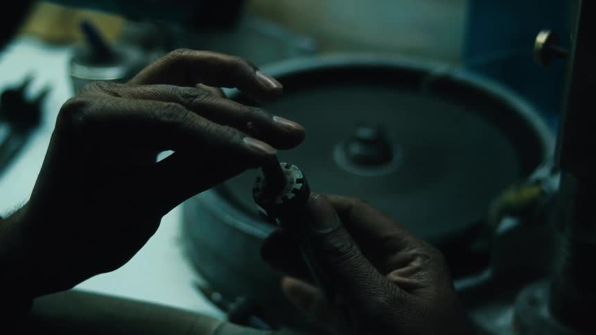 A closeup of a persons hands using a rotary tool to carefully grind and shape a piece of metal