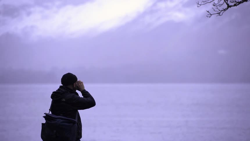 Person observing the landscape with binoculars by the lakeside