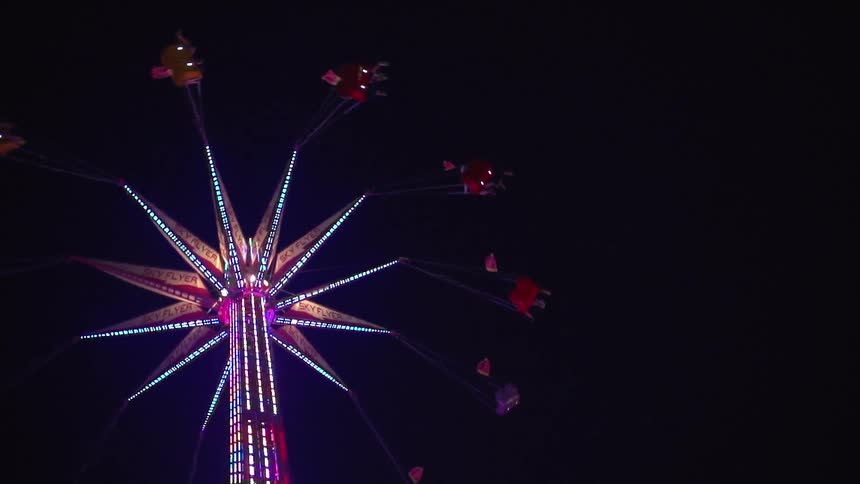 A ferris wheel is lit and spinning on a dark night