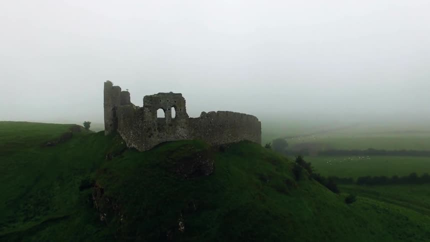 A rundown building on top of a large hill that is very green