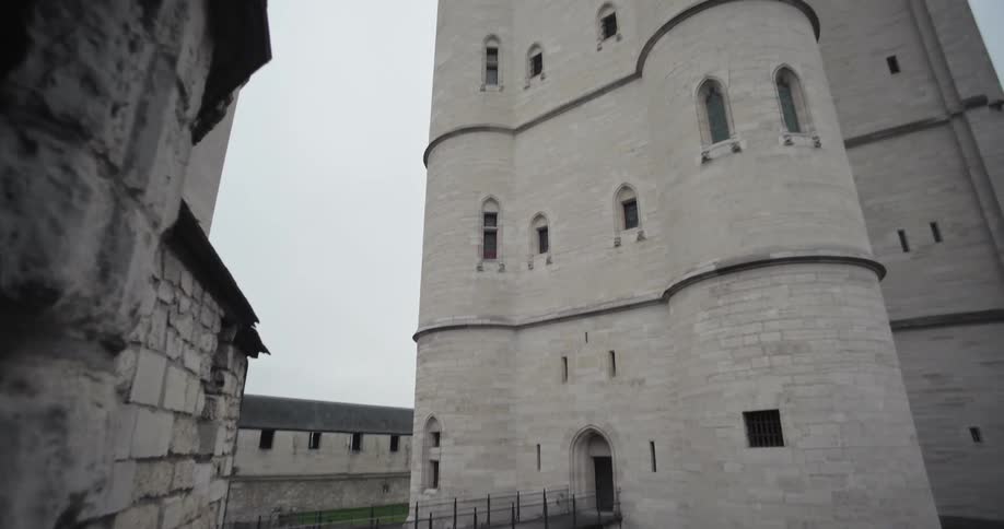 The video shows a medieval castle with a bridge leading to a large round tower the camera slowly tilts up to reveal the full height of the tower against a cloudy gray sky