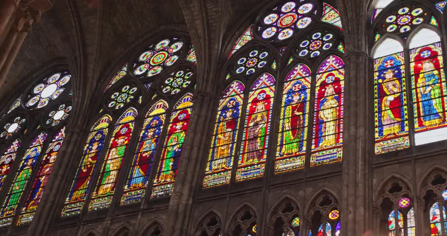 A closeup of the interior of a large church shows multiple rows of ornate stainedglass windows depicting religious figures in various colorful patterns