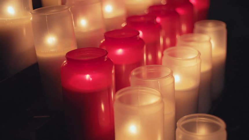 Rows of red and white votive candles in glass jars flicker gently casting a warm glow in a dark reverent space