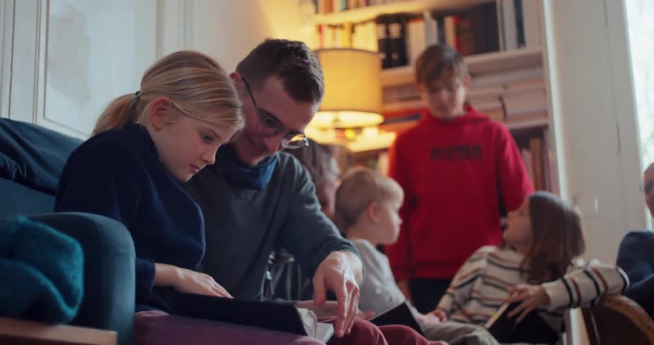 A father sits with his kids on a couch in the living room as they all read the bible together