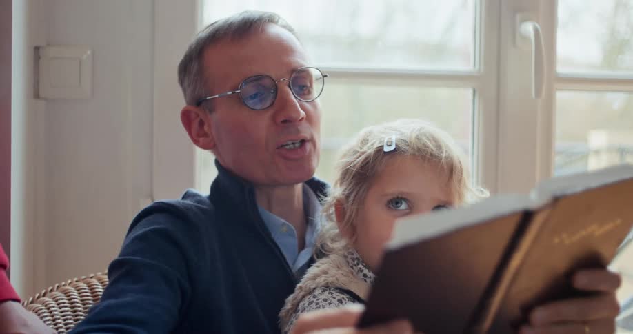 Father sitting with his little daughter on his lap reading a book