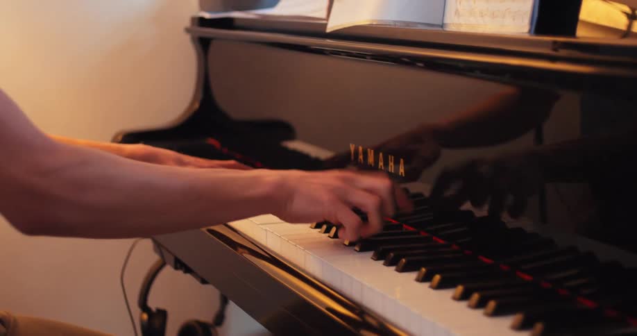 A young mans hands play a grand piano and then he is seen concentrating on the music
