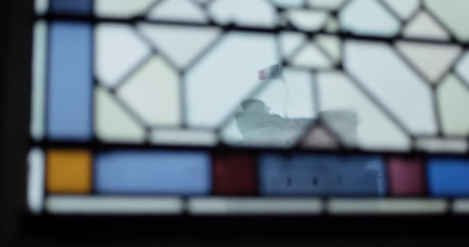 A view through a stained glass window with a focus on the geometric pattern the camera slowly racks focus from the stained glass to a building with a french flag flying on top which is now blurred and out of focus