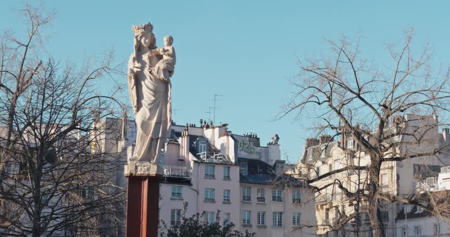 A shot of a statue trees on the back city buildings and a clear blue sky in the background