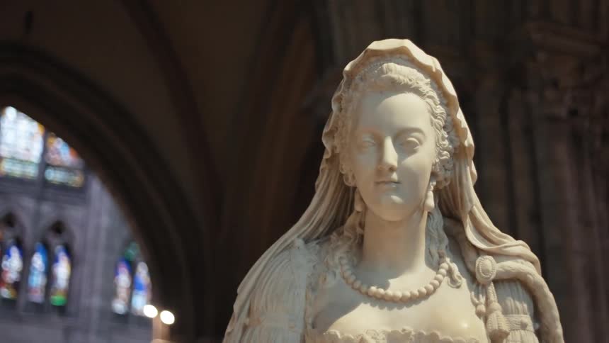 A statue of marie antoinette stands in front of a church at midday