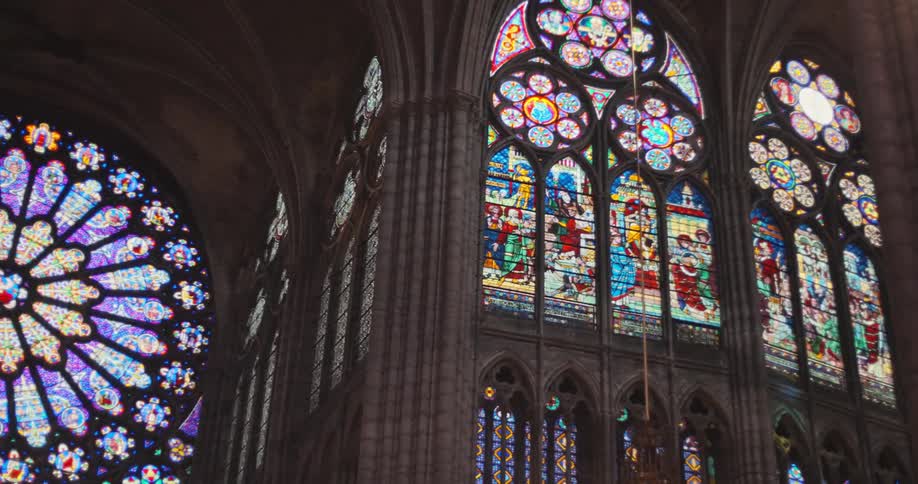 A camera pans slowly across the interior of a large old church revealing a series of towering stainedglass windows that show intricate religious scenes and a large circular window with a colorful pattern