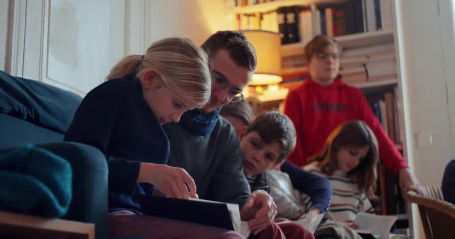 A father sits with his kids on a couch in the living room as they all read the bible together