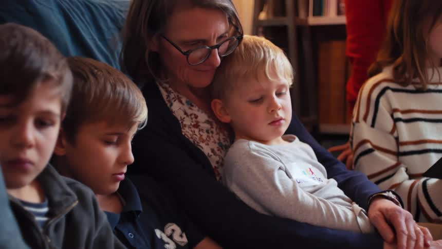 Woman sitting on a sofa with several other children who are reading books
