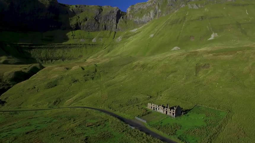 An aerial view of a run down home in a hilly open green field