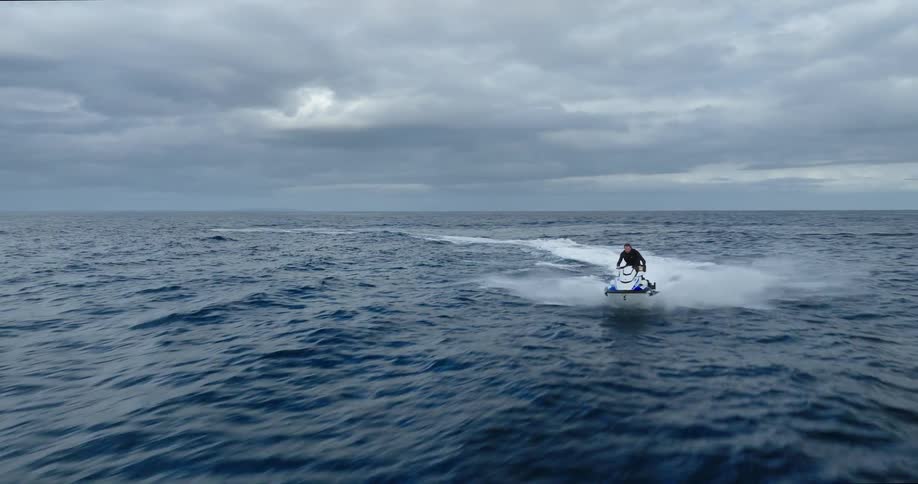 A person riding a jet ski at top speed in the ocean at midday on a cloudy day