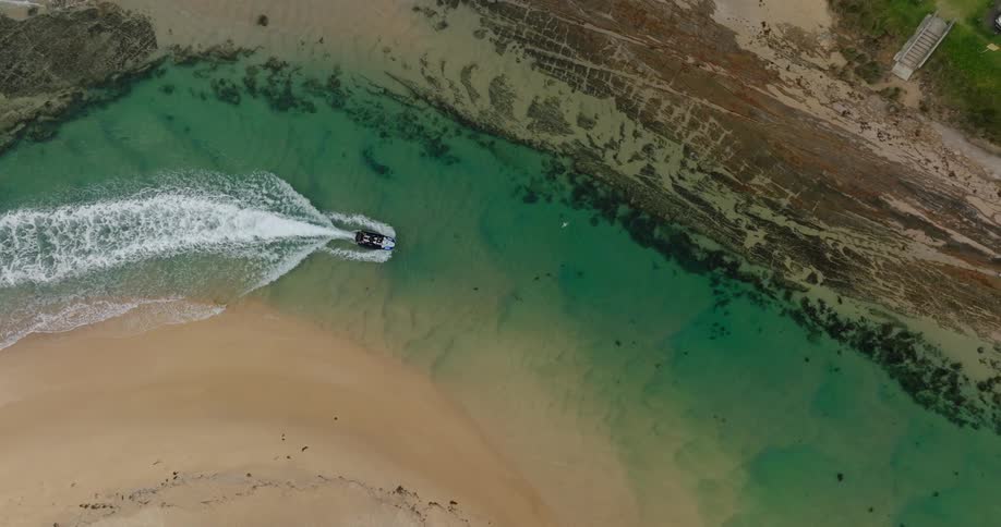 A boat speeds through a narrow turquoise channel between sandy shores and rocky terrain