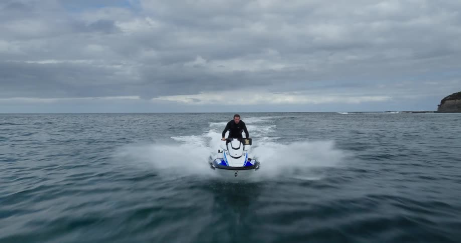 Man riding a jet ski at high speed across the ocean on a cloudy day