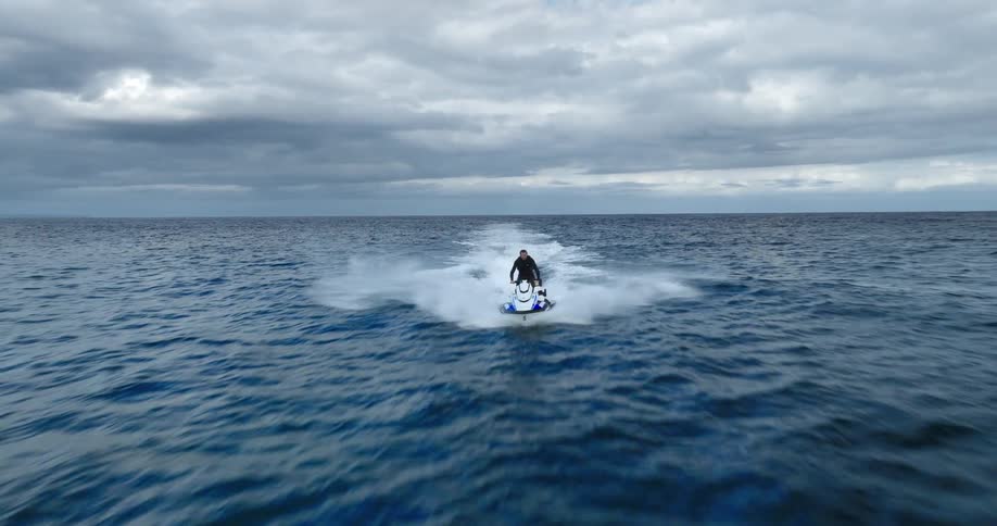 A lone person on a jet ski speeds across the wideopen ocean leaving a white wake behind them the sky above is overcast with heavy dark clouds