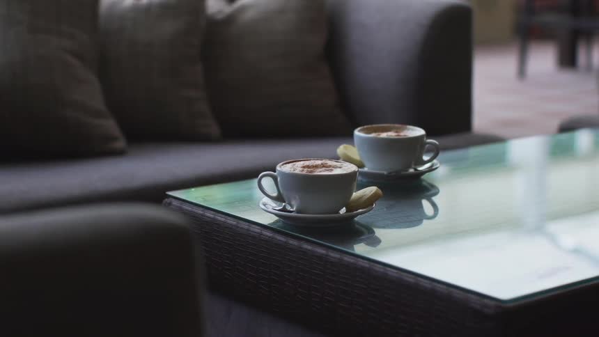 Two cappuccino cups sit on a coffee table