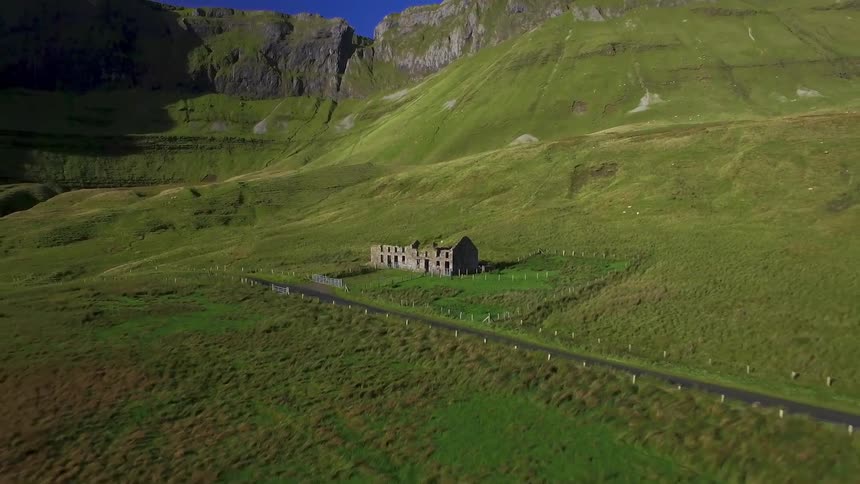 A zooming out view of a run down house surrounded by open green land