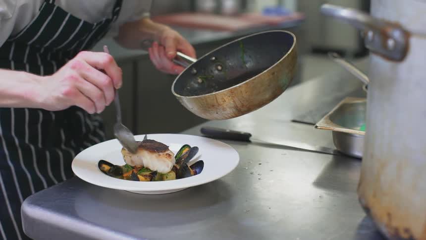 A person scooping sauce from a pan and placing it over some food on a plate