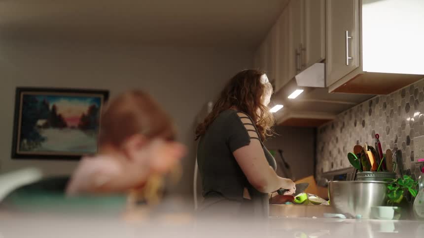 A woman with a headband and long brown hair is smiling while working in a kitchen she is standing at a counter with kitchen utensils in a jar and a silver bowl to her right