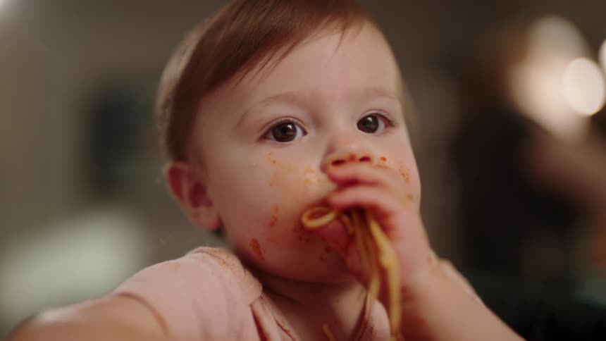 Baby with sauce on the face eating spaghetti with hands