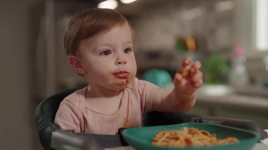 Little girl sitting eating pasta with sauce with her hand